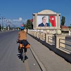 Ein Radfahrer fährt eine Straße entlang. Rechts ein großes Plakat mit einem Mann vor der Flagge Aserbaidschans.