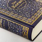 "Der Koran" steht auf dem Buchrücken und Cover eines reich verzierten Buches mit goldenen Mustern.
