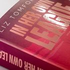 „IN HER OWN LEAGUE“ in großen Buchstaben, „LIZ TOMFORDE“ in kleineren. Dunkelrote Buchabdeckung mit Wolkenkratzern.