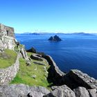 Eine steinige Küstenlandschaft mit grünen Grasflächen, im Hintergrund ein blauer Ozean und eine kleine felsige Insel.