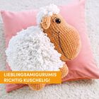Lieblingsamigurumis: richtig kuschelig! Ein gehäkeltes Schaf auf einem rosa Kissen auf einem hellen Teppich.
