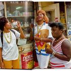 "New York's Lottery" ist auf einem Fenster zu sehen. Drei fröhliche Menschen stehen draußen, zwei trinken Getränke.