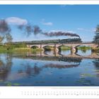 Text: Juni. Eine Dampflokomotive zieht Rauch hinter sich über eine Brücke. Darunter klarer Fluss mit Spiegelung.