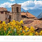 "juni" steht in der linken Ecke. Gelbe Blumen blühen vor einem ruhigen Dorf mit alten Steinhäusern in einer bergigen Landschaft.