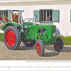 „Juni“ steht unten links in Großbuchstaben. Ein grüner Traktor mit roten Rädern vor einem Haus mit grünen Fensterläden.