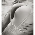 "Juni" steht geschrieben. Eine sinnliche Szene zeigt Hände mit Perlenkette auf Spitze und Haut, akzentuiert in Grautönen.