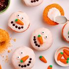 Cupcakes mit Schneemann-Gesichtern aus Zuckerguss, Schokoladenaugen und Möhrennasen. Löffel verteilt Zuckerguss.
