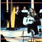 Der Text erwähnt den Sieg einer jungen Frau beim Eurovision Song Contest. Drei Leute mit Instrumenten auf einer Bühne.