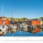 Kalendertext: Juni 2023. Boote liegen vor bunten Holzhäusern am Wasser. Klare Spiegelung, blauer Himmel.
