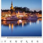 Juni 2027 Kalender. Abendhafen mit beleuchteten Gebäuden und Schiffen. Oben Kirchturm, darunter ruhiges Wasser mit Spiegelungen.