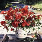 Eine üppige Blumenvase mit leuchtend roten Mohnblumen und grünen Blättern auf einem Holztisch draußen.