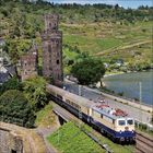 Eine Lokomotive mit der Nummer "103 113-7" fährt an einem alten Burgturm nahe eines Flusses vorbei.