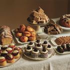 Verschiedene Gebäcksorten auf einem Tisch, darunter Kuchen, Muffins, Cupcakes mit Erdbeeren und Brownies, appetitlich arrangiert.