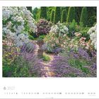 6 2027. Garten Schönwetter, Rosendal, Deutschland. Üppiger Garten mit Blumen, Büschen und Skulptur in der Mitte.