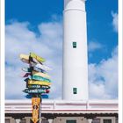 Schriftzüge: "KEY WEST 878 KM", "CUBA 218 KM". Leuchtturm vor blauem Himmel mit Wegweisern und einem weißen Gebäude.