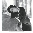 Coco Chanel, berühmte Designerin, sitzt nachdenklich an einem Tisch. Sie trägt elegante Kleidung und schmuckvolle Accessoires.