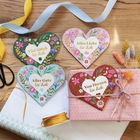 Herzförmige Karten mit „Viel Glück für dich“ und anderen Botschaften, auf Holzuntergrund mit Bändern, Geschenk und Trockenblumen.