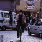 Texte: Kolb's, Polizei, Friedrichstraße. Ein Mann fährt Fahrrad, im Hintergrund ein Polizeiwagen und Polizisten.