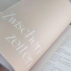 „Zwischenzeiten" steht groß auf einer aufgeschlagenen Buchseite. Daneben beginnt ein Text in kleineren Buchstaben.