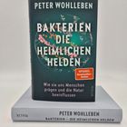 Buchcover: „BAKTERIEN DIE HEIMLICHEN HELDEN“, Autor: Peter Wohlleben. Darunter liegt das Buch, Rücken zeigt denselben Text.
