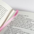Ein aufgeschlagenes Buch mit einem rosa Leseband. Textpassagen zeigen Dialoge mit Ausdrücken wie: „Quatsch“, „Klar, Mann.“