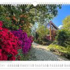Juni. Azaleen und Rhododendrenblüte. Ein gepflasterter Weg führt an bunten Blüten und einem modernen Holzhaus vorbei.