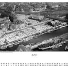 "JUNI" und "Flugbild vom Deichdomarkt und den Deichhallen." Luftaufnahme eines Hafens mit vielen Gebäuden und Schiffen.