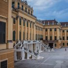 Palastarchitektur mit hohen, gelben Fassaden, verzierten Fenstern und breiten Treppen in einem weitläufigen Hof.