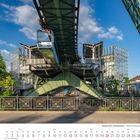 Wuppertaler Schwebebahn über Bahnhof. Juni 2027 Kalender unten. Architektur aus Glas und Stahl, Bäume, blauer Himmel.