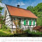 „6 2027. Wermelskirchen. Fachwerkhaus in Zumühle.“ Ein Fachwerkhaus mit roten Dachziegeln inmitten grüner Natur.