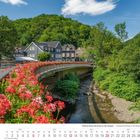 Schloss Burg und Burg an der Wupper. Juni 2027 Kalender. Brücke mit roten Blumen über einem Fluss, umgeben von grüner Natur.