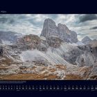 03 März. Die Seiserer Sonnenuhr mit Gipfeln der Dolomiten. Karge Landschaft mit markanten Felsformationen unter wolkigem Himmel.