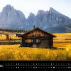 Text: „Dolomiten 06“. Eine Holzhütte steht in einer sonnigen Berglandschaft mit steilen Felsen im Hintergrund.