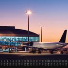 Kalenderanzeige für Juni mit Wochentagen und Zahlen. Flugzeug an einem Terminal bei Sonnenuntergang im Hintergrund.