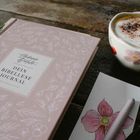 „Dein Bibellese Journal“ auf einem rosa Buch, Tulpe, Kaffee mit Milchschaum in geblümter Tasse, Zeichnung einer Blume.