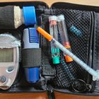 Ein offenes Etui mit Blutzuckermessgerät, Teststreifen, Lanzette, Insulinampullen und Spritze, alles sicher verstaut.