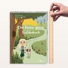 „Der kleine grüne Fußabdruck“ zeigt ein Kind und Hund auf Weg, umgeben von Bäumen, grüner Wiese und Windrädern.