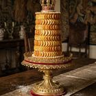 Ein Turm aus Keksen mit einer goldenen Krone oben, auf einem verzierten goldenen Sockel in einem eleganten Raum.