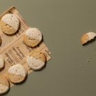 Halbe Kekse in weißer Glasur auf altem Zeitungspapier. Krümel verstreut auf grünem Hintergrund.