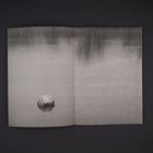 Keine Texte sichtbar. Schwarz-weißes Foto eines Balls, der auf einem ruhigen Wasser schwimmt.