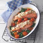 Ein ovaler Teller mit Lachs, überbackenem Käse, Kirschtomaten und Spinat, daneben liegt ein blau-weiß kariertes Geschirrtuch.