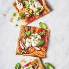 Drei rechteckige Pizzastücke mit Tomaten, Ricotta, Basilikum und Pesto auf hellem Untergrund.