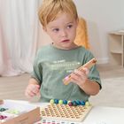 Ein Kind spielt mit bunten Kugeln und einem Holzbrett. Auf dem T-Shirt steht "THE JOURNEY STARTS". Im Hintergrund sind Farbvorlagen.