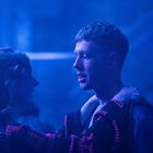 Es gibt keinen sichtbaren Text. Ein junger Mann und eine Frau stehen in einem blauen Licht, sie hält ihn an den Schultern.