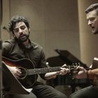 Zwei Männer spielen Akustikgitarren und singen in einem Studio. Im Hintergrund steht ein Klavier.