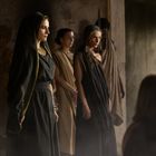 Keine erkennbaren Texte. Vier Personen in antiker Kleidung, zwei davon tragen schwarze Gewänder, die anderen beige.