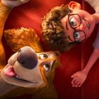 Ein Junge mit Brille liegt lachend neben einem fröhlichen Hund auf einem roten Sofa und trägt ein T-Shirt mit einem Logo.