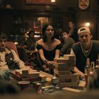 Personen in entspannter Bar-Atmosphäre, spielen Jenga. Auf dem Tisch stehen Getränke und Spiele.