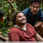 Vier Personen im Dschungel; eine Person sitzt, lächelt und schaut nach oben, umgeben von dichten grünen Blättern.