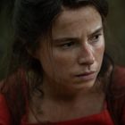 Keine Texte zu erkennen. Eine Frau mit ernstem Blick und zerzaustem Haar in einem roten Kleid.